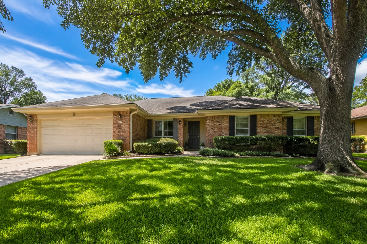 A charming single-story brick ranch-style starter home in a quiet Houston suburb with a green lawn.