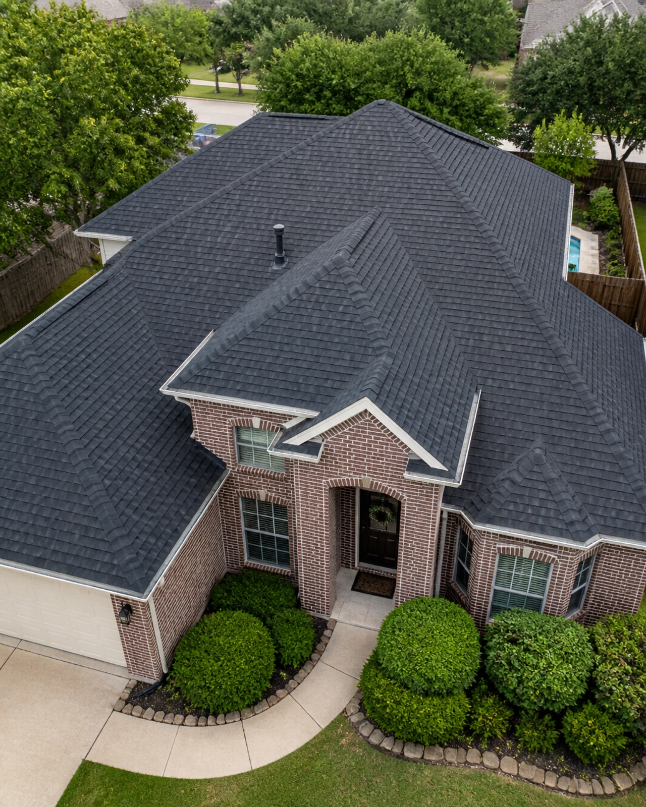 A close-up drone shot of a new architectural shingle roof with clean, debris-free gutters.