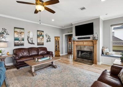 Living room interior with ceiling fan, fireplace, and brown leather sofa featured in Galveston, Texas property.